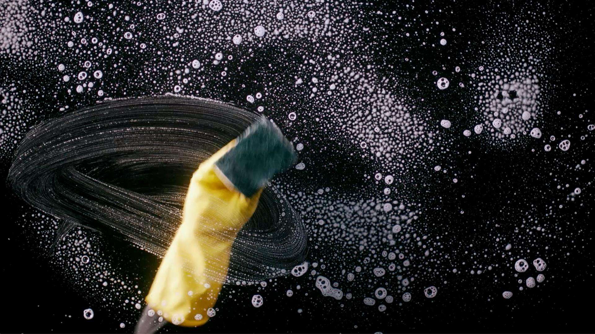 View from below, showing a hand with a glove cleaning the cooktop with a sponge