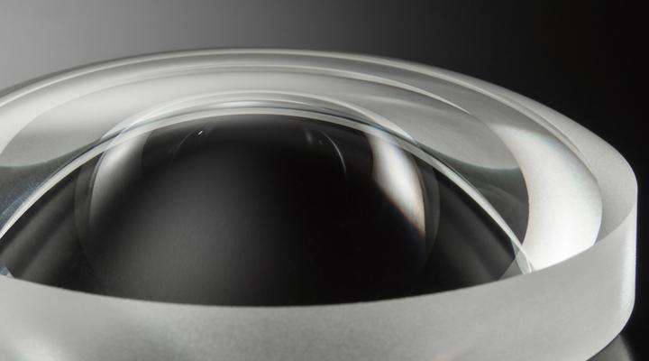 Close-up of clear aspherical lens by SCHOTT on a dark background with reflection on their surfaces