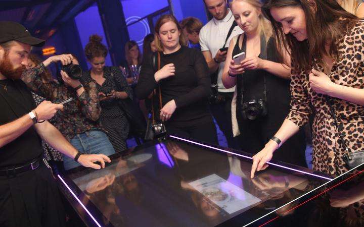 A crowd of people around a concept table with a FUSICS® touch surface experiencing the high-tech concept kitchen