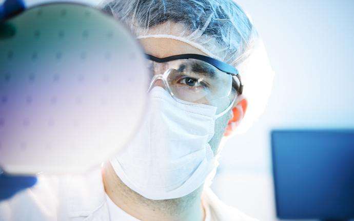 Scientist in a laboratory inspecting a glass wafer