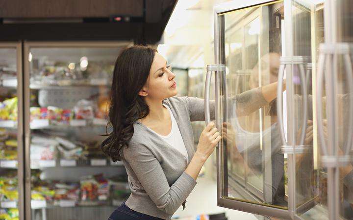 Woman opening a freezer door in a supermarket