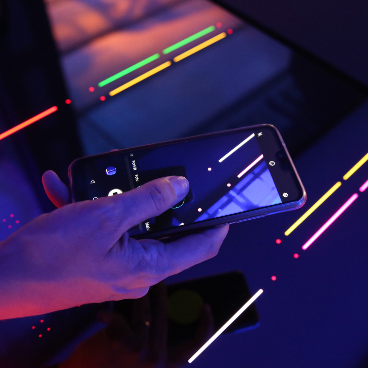 A hand with a mobile phone in photo-mode over a glass-ceramic with colored illuminated light elements