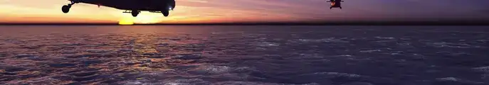 Helicopters flying across an ocean into the sunset