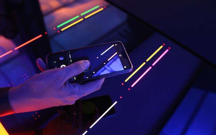 Hand holding a smartphone over a SCHOTT CERAN EXCITE® cooktop with colored lighting