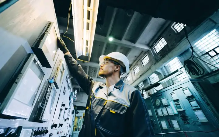 Mann in Arbeitskleidung blickt auf Display in Industrieanlage