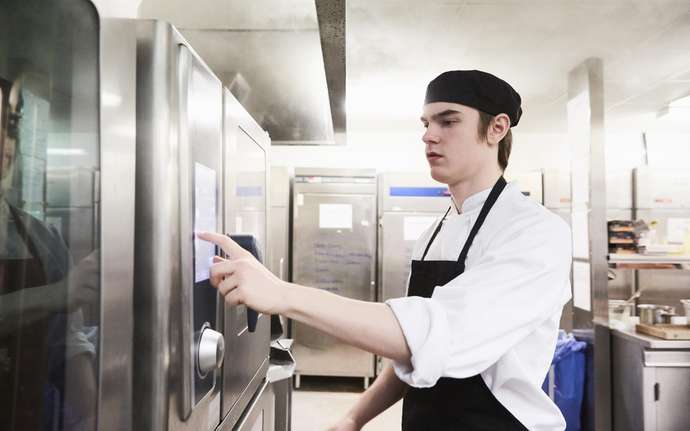 Young chef operating a professional oven in a commercial kitchen