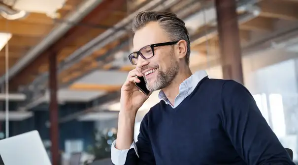 Man in glasses in business office on phone while working on laptop