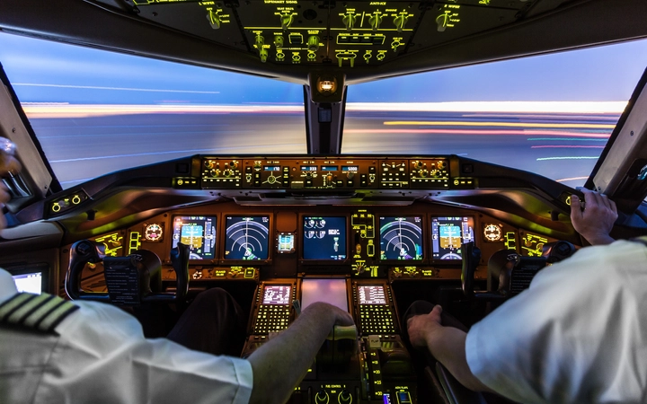 Innenansicht eines Flugzeug-Cockpits mit beleuchteten Bedienelementen und Anzeigen