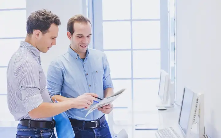 Two young men discuss information on a publication