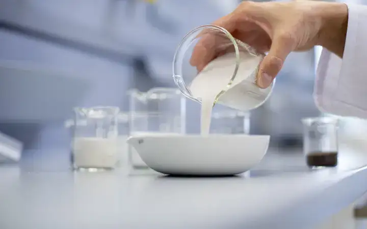Scientist pouring glass powder into a ceramic bowl in a laboratory