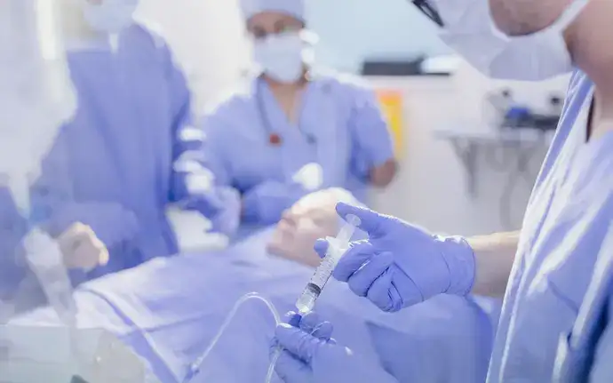 Anesthetist with a syringe injecting anesthetic into IV drip in the operating room