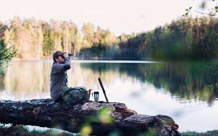 Man looking through a pair of high-powered binoculars on a lake