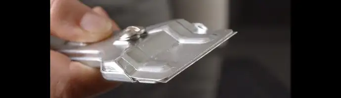 A hand holds a metal cleaning scraper to clean the glass-ceramic cooktop