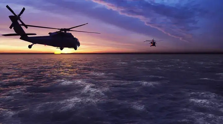 Helicopters flying across an ocean into the sunset