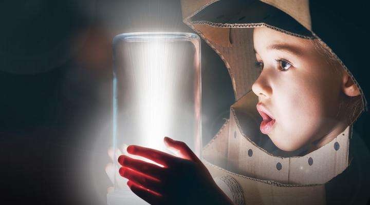 Young boy looking at a glass jar full of light